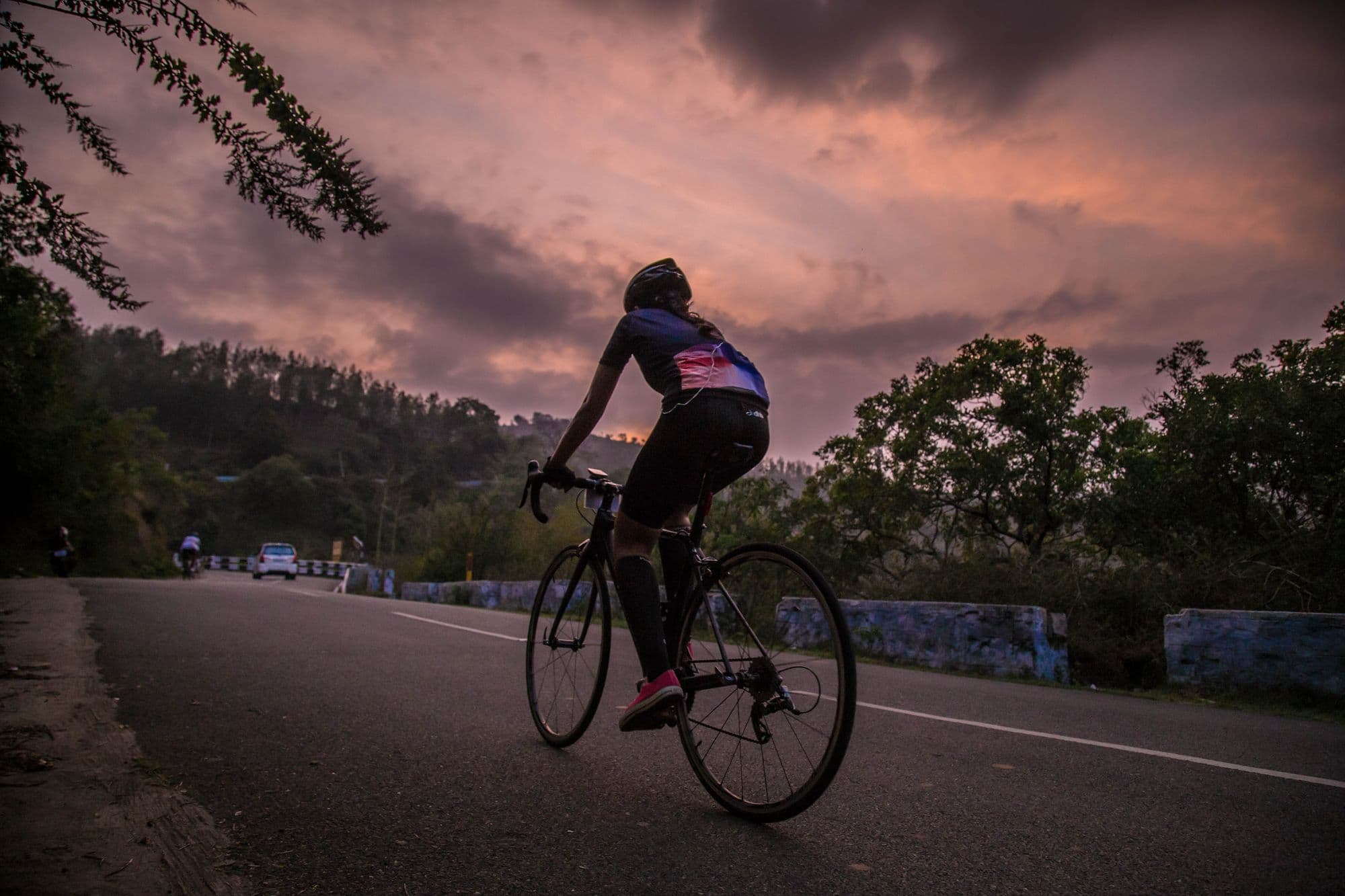 Ciclista numa estrada de serra ao entardecer, com céu rosado e nuvens carregadas