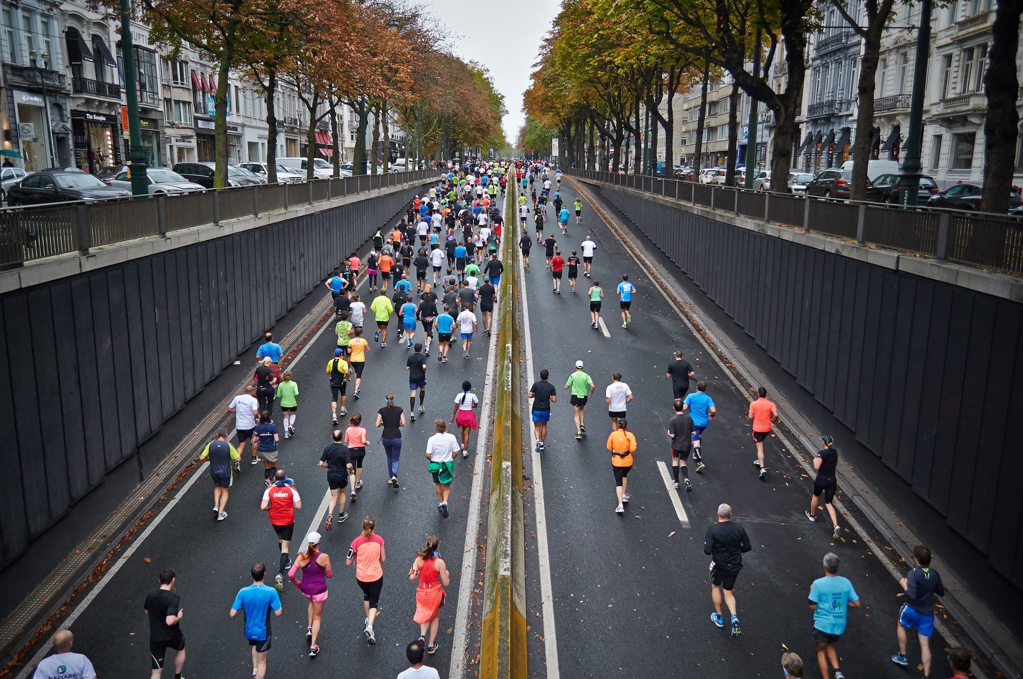 Vista do alto de uma avenida arborizada tomada por corredores durante uma maratona
